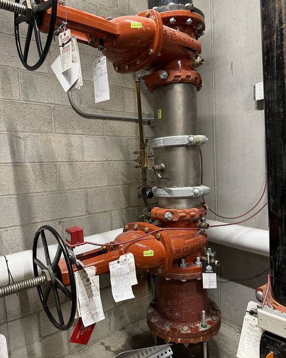 Orange backflow assembly with two large handwheel valves and tags hanging from it