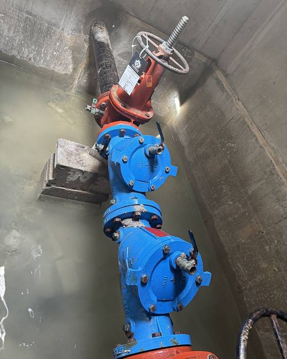 Blue backflow assembly with a red handwheel valve inside a below-grade concrete vault