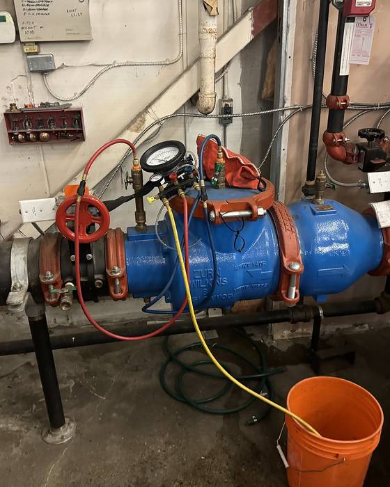 Large blue backflow preventer with red shutoff valves, a hose and an orange bucket