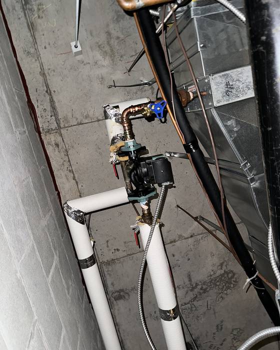Circulator pump with copper fittings on white insulated piping beside a concrete wall