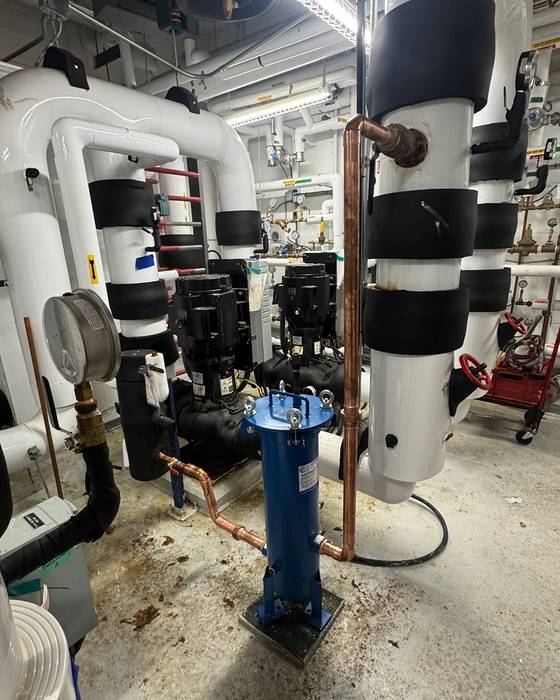 Blue filter vessel on copper piping in a mechanical room with pumps