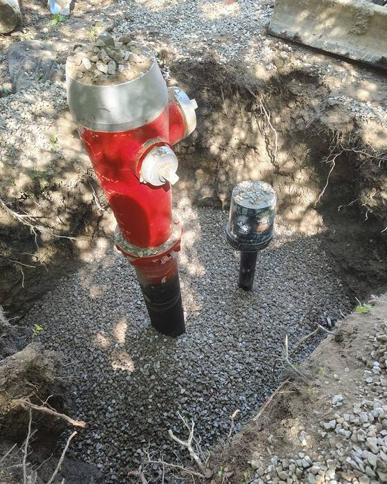 New red fire hydrant installed in an excavation with gravel