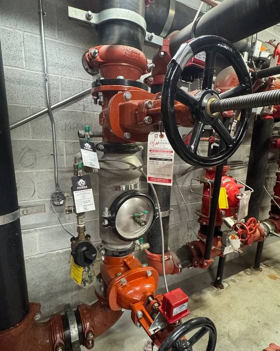 Fire sprinkler riser and backflow assembly with large black handwheel valves and PANDA service tags