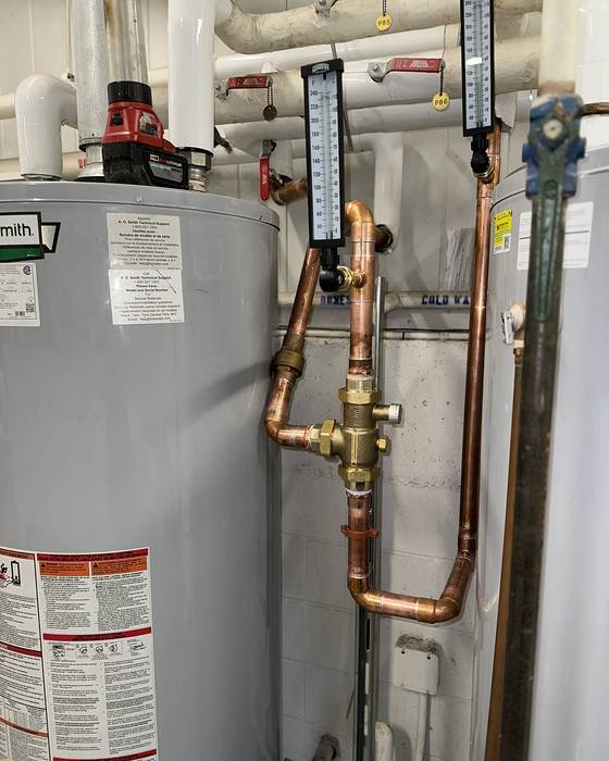 Gas water heater with two thermometers and copper piping around a mixing valve