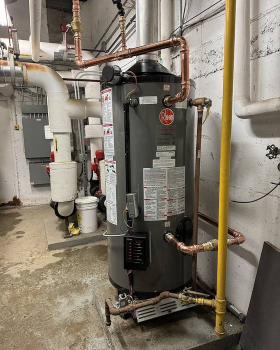 Large gas-fired water heater with copper piping and a yellow gas line in a mechanical room