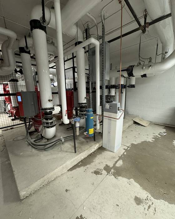Mechanical room with pumps on a concrete pad and large white insulated piping