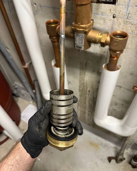 Hand holding a removed mixing valve cartridge in front of the installed mixing valve