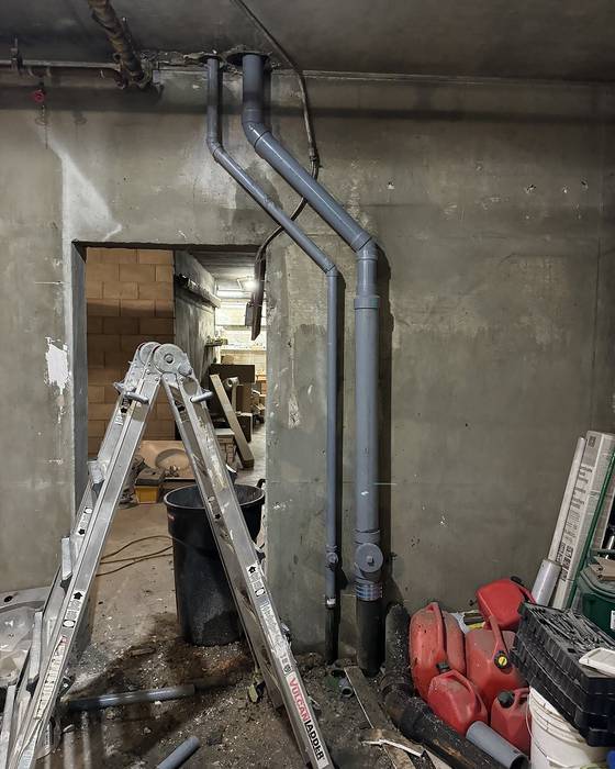 New grey drain piping running up a concrete wall next to an open doorway