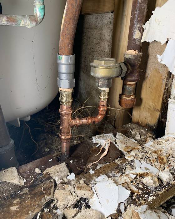 Opened wall with old rusted pipe tied into new copper piping with press fittings and a small new valve assembly