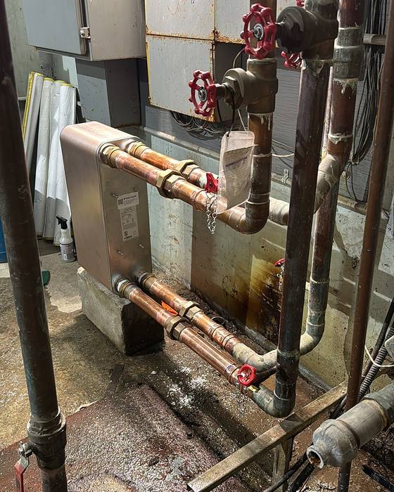 Small heat exchanger with copper piping and red valve handles in a mechanical room