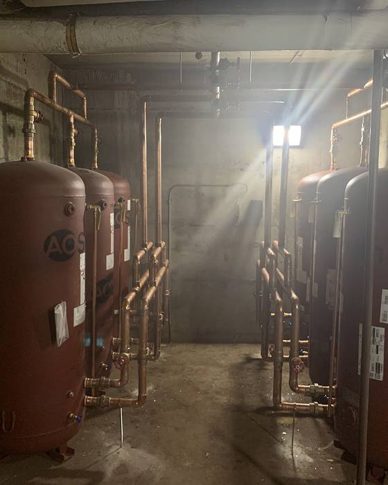 Row of red A. O. Smith storage tanks with copper manifold piping in a mechanical room