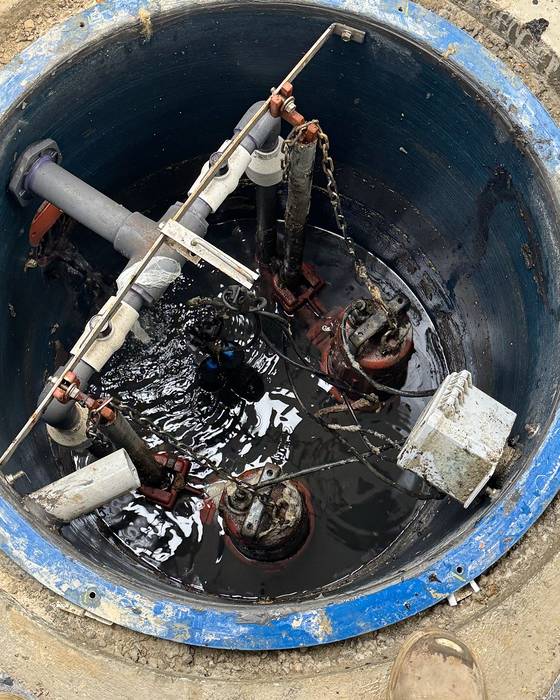 Looking down into a sewage pit with submersible pumps on guide rails