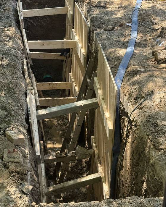 Timber-shored excavation trench with a sewer or water line