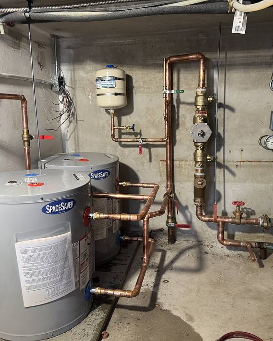 Two grey storage water heaters with copper piping, gauges and a small expansion tank