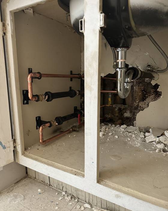 Cabinet opened up under a sink showing new copper piping and shutoff valves
