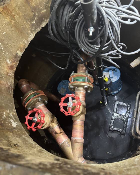 Looking down into a valve chamber with two red handwheel valves on copper piping and cables above