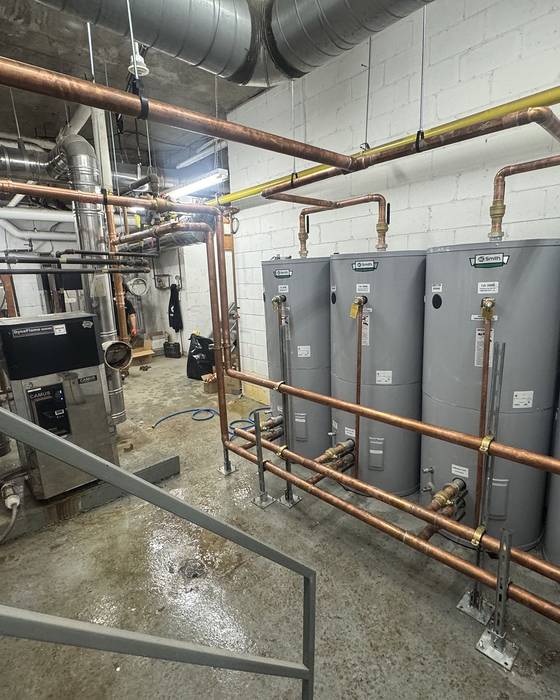 Bank of four storage water heaters piped with a copper manifold in a mechanical room